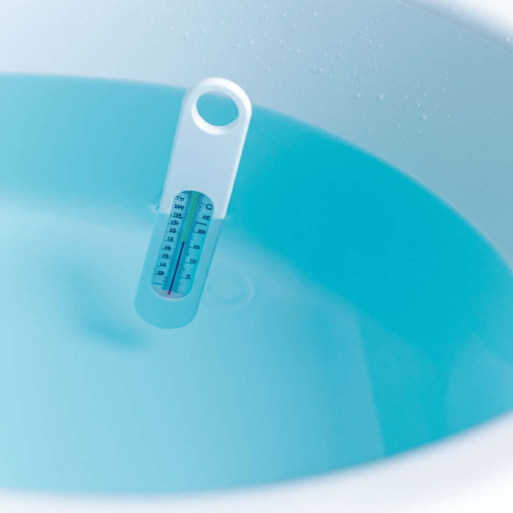 Witte analoge badthermometer met ronde hoeken in blauw badwater voor veilige babybadtemperatuur
