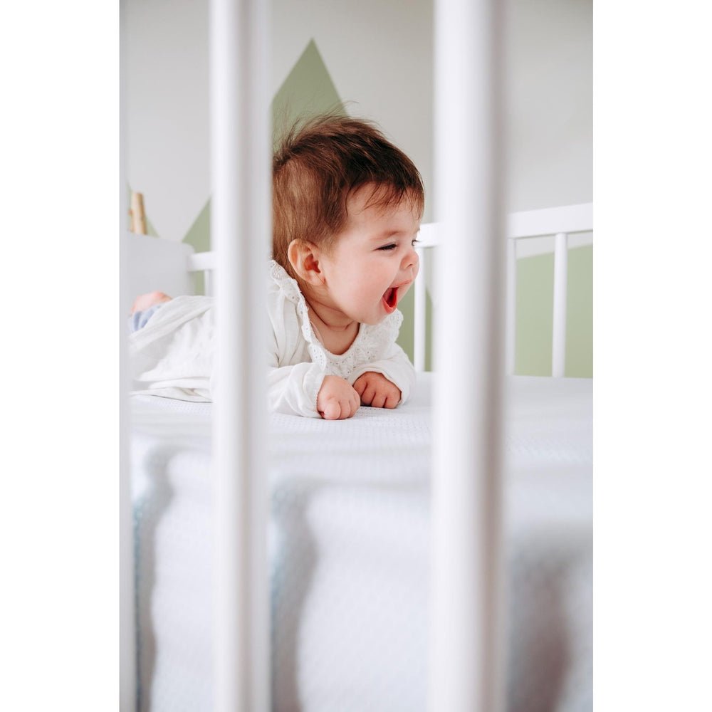 Baby slaapt op wit AirgoSafe hoeslaken met geperforeerde textuur in wieg