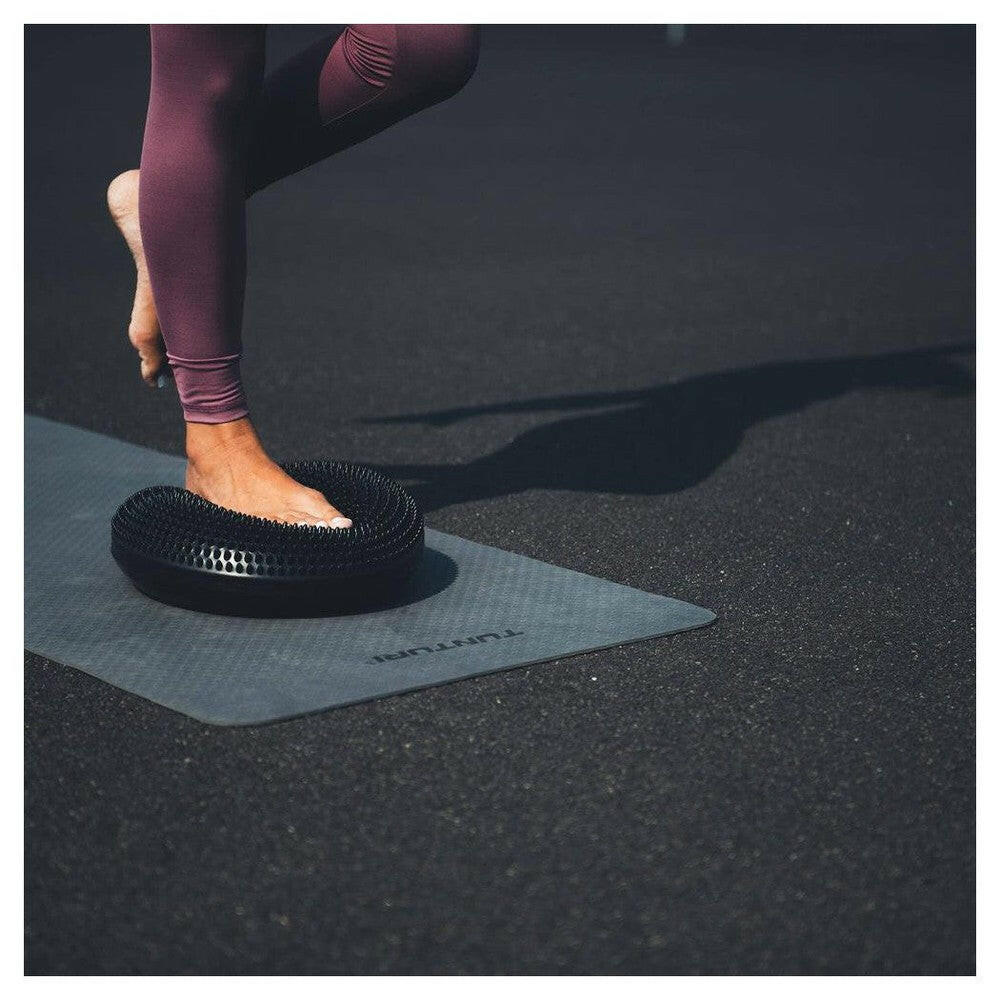 Persoon staat op Tunturi Air Stepper Pad zwart op yogamat voor evenwicht