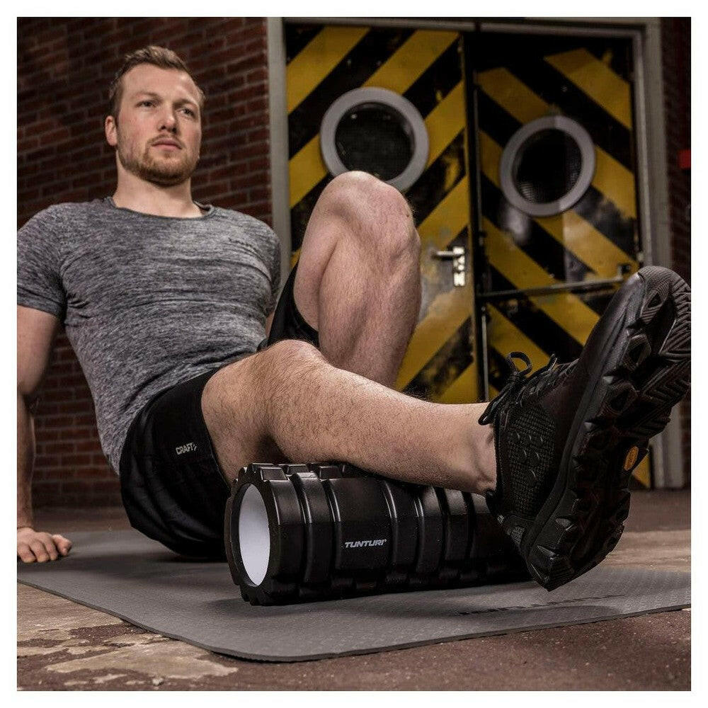 Man gebruikt zwarte Tunturi foamroller voor dijspierverlichting tijdens training