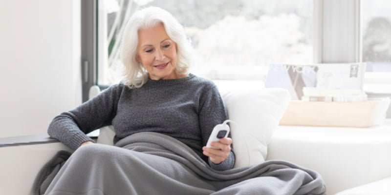 Foto van oudere dame met elektrische deken op de bank, voor een blog over warmte dekens bij reuma of atritits