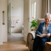 Oudere vrouw in een rustige woonkamer met hulpmiddelen die zelfstandig en veilig thuis wonen ondersteunen.