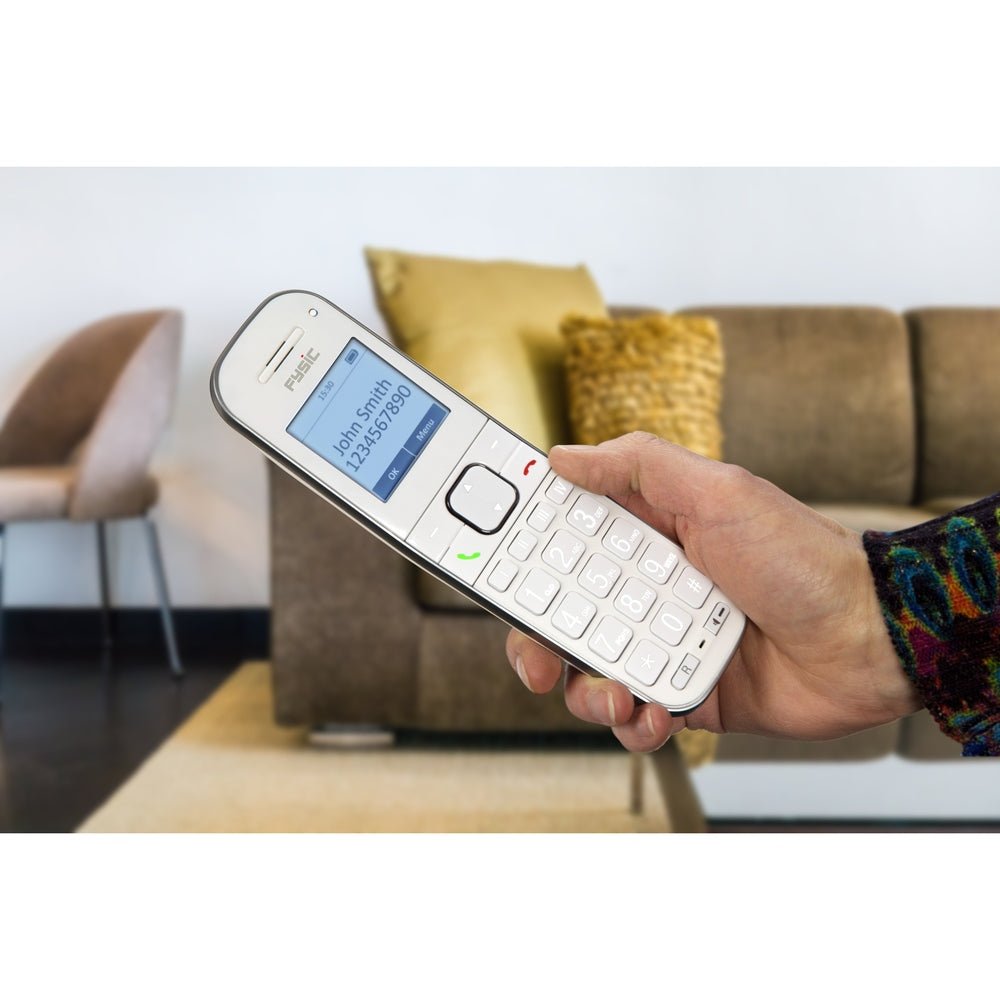hand houdt witte Fysic seniorentelefoon vast in woonkamer met groene en rode knoppen