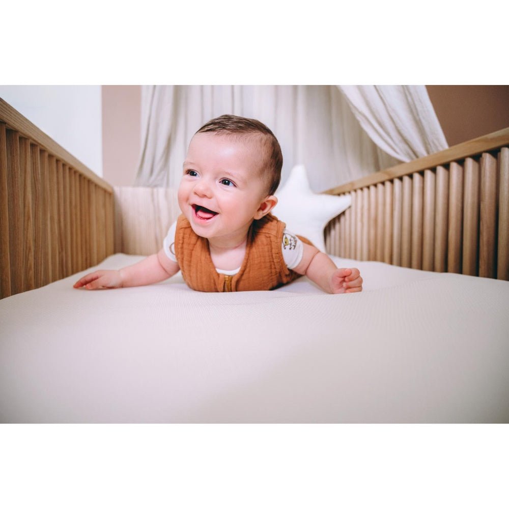 Baby op witte waterafstotende matrastopper in wieg