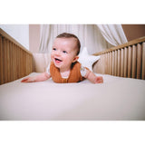 Baby op witte waterafstotende matrastopper in wieg