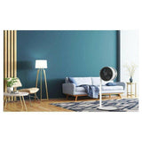 witte ventilator in woonkamer met donkerblauwe muur, grijze bank en geometrisch tapijt