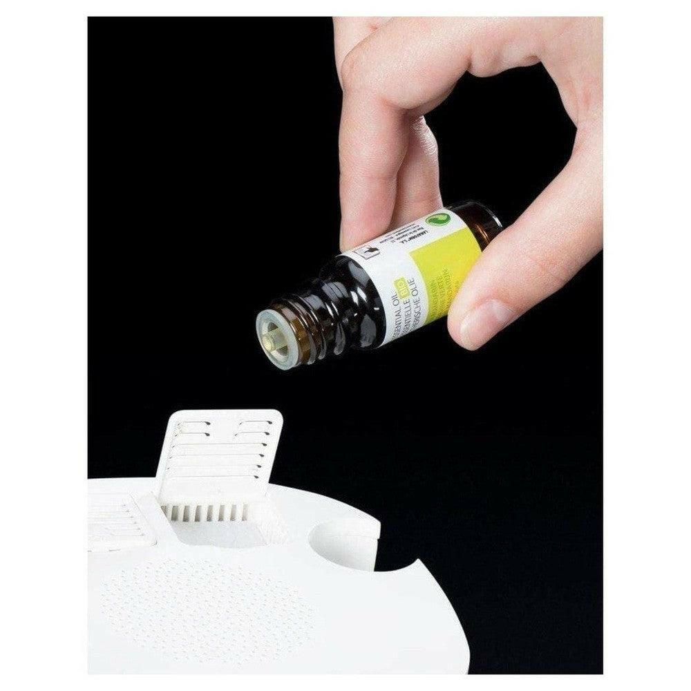 Hand vult Lanaform wake-up light met essentiele olie uit bruin flesje
