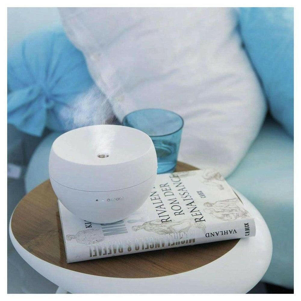 Witte bolvormige diffuser met zichtbare nevel op boek en bijzettafel in zachte woonomgeving