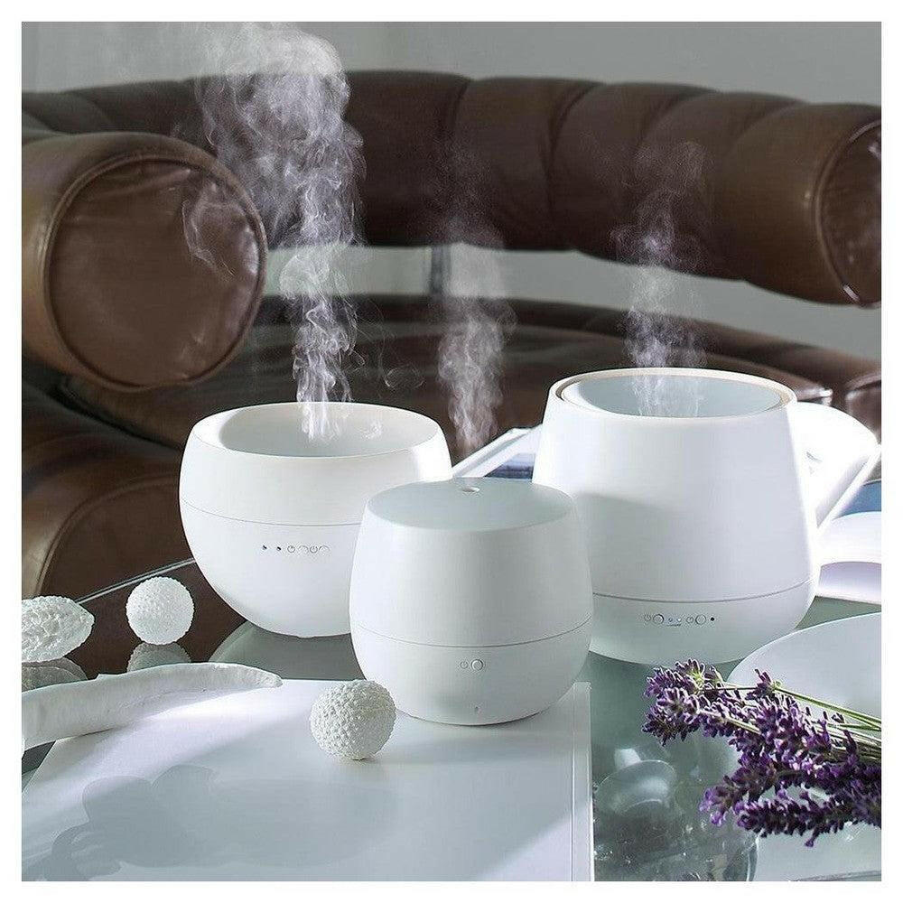Actieve witte aroma diffusers met nevel op glazen tafel bij lederen fauteuil en lavendel
