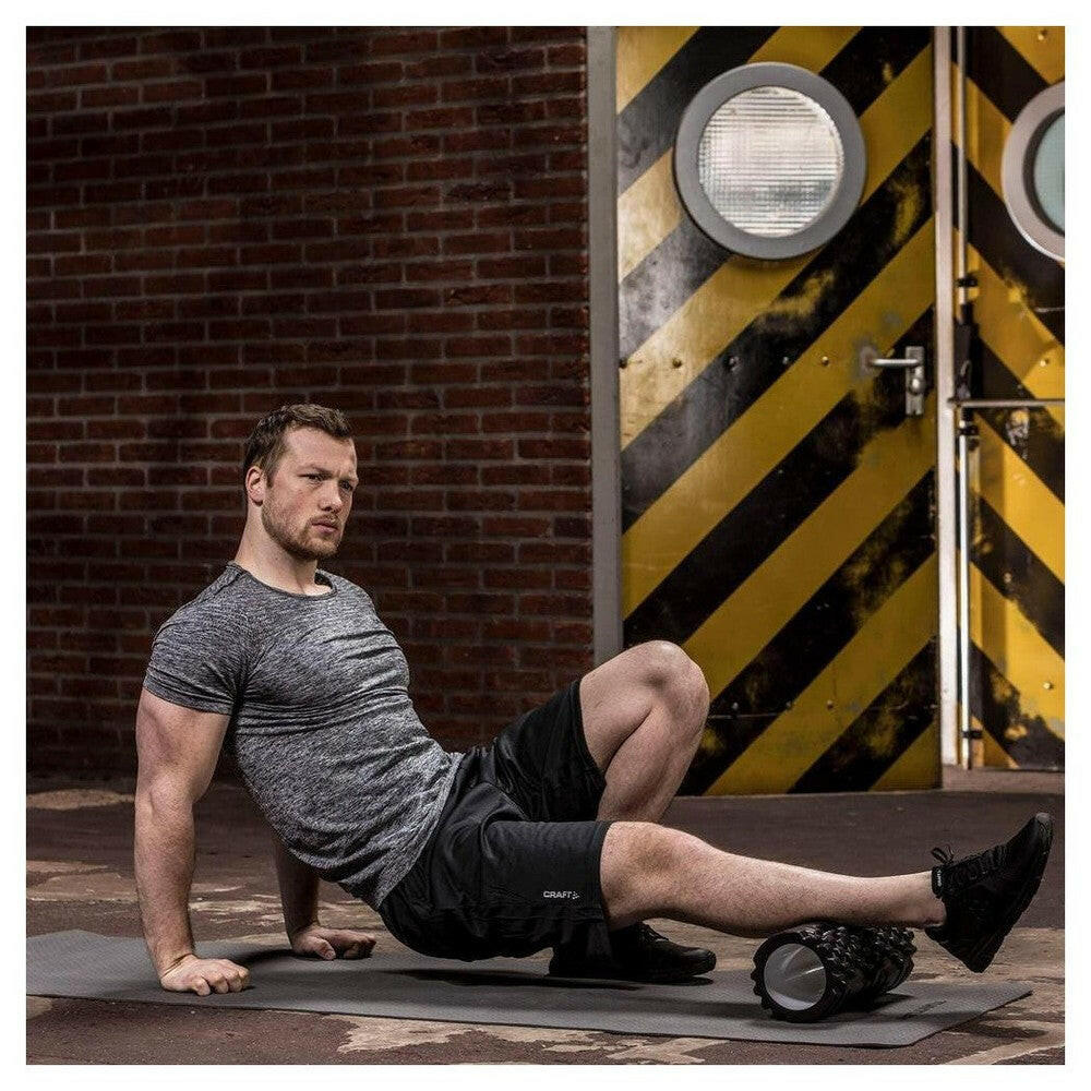 Man gebruikt zwarte Tunturi foamroller met bloktextuur voor spierherstel
